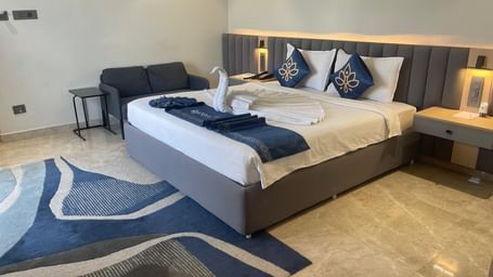 Well lit bedroom at Hotel Kyzen HiTech City with a king bed, blue carpet and a sitting area.